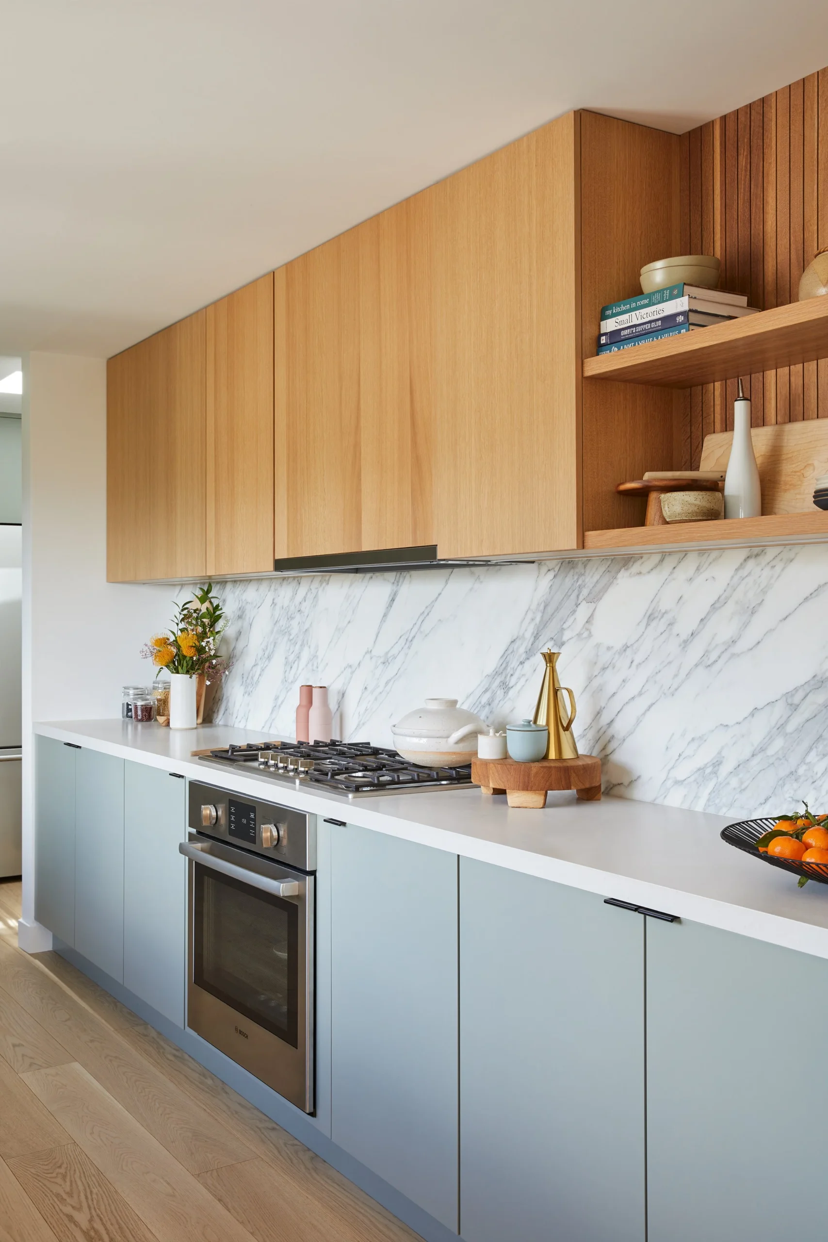 Modern kitchen renovation by Quay Construction featuring two-toned blue base and oak upper cabinets, a marble backsplash, and built-in Bosch appliances.