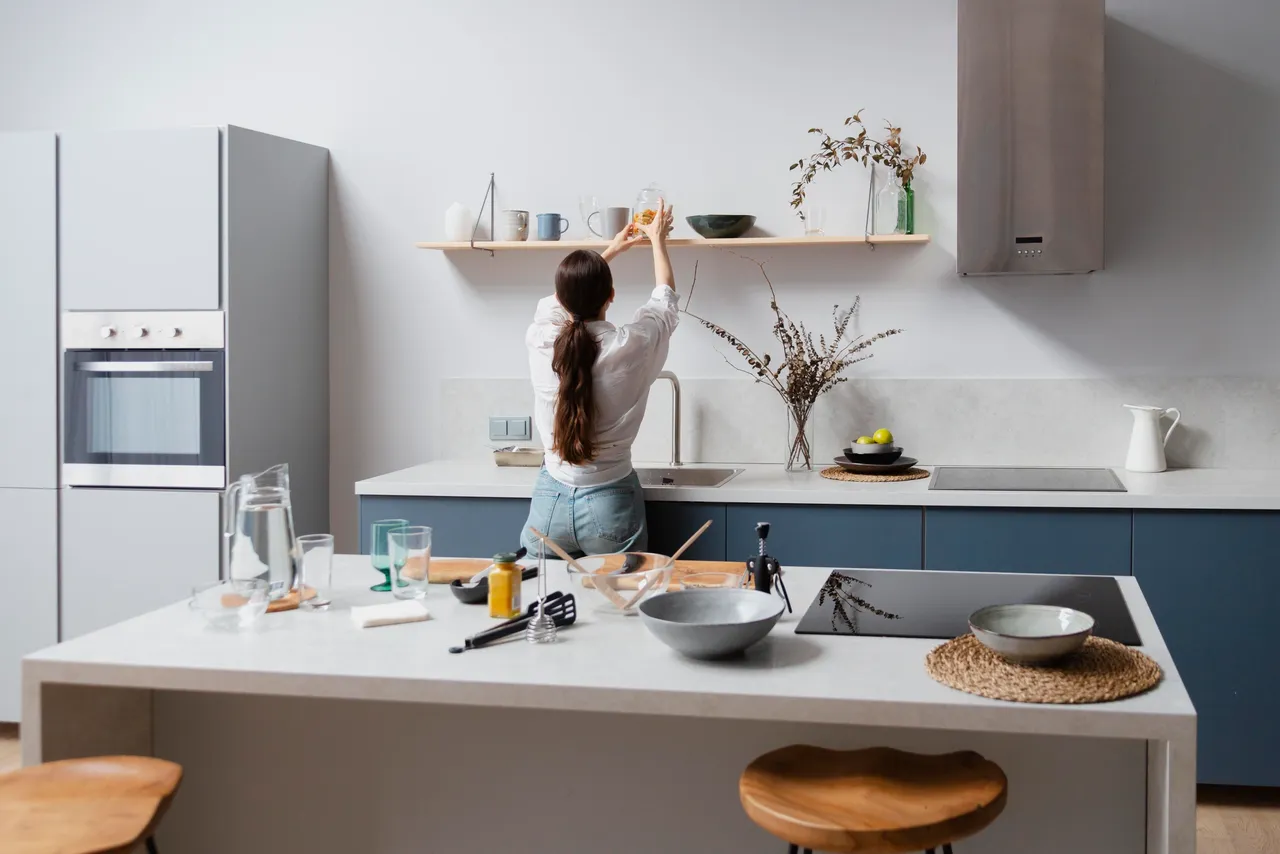 Woman working in open kitchen space, stools at a kitchen island, plants, wooden shelving