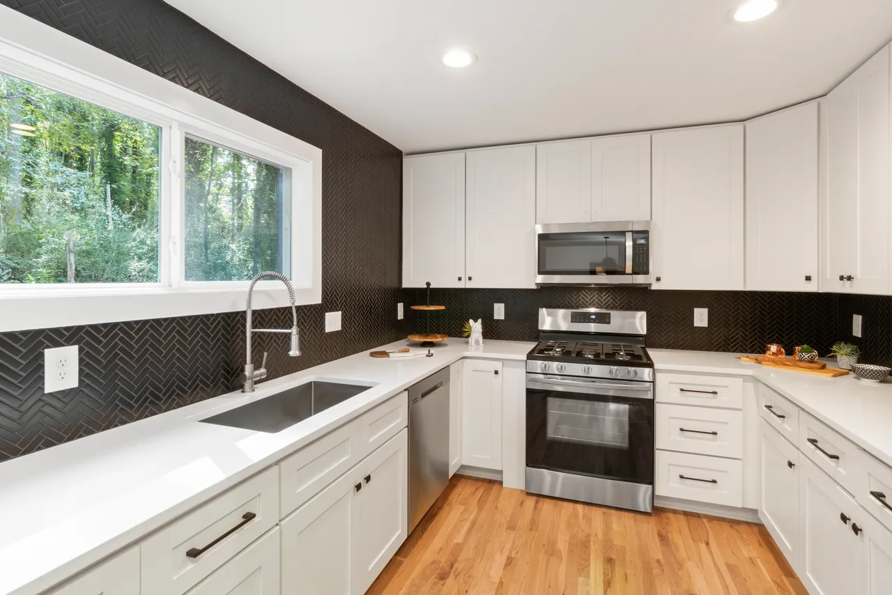 A white kitchen with hardwood floors and black tiled backsplashes.