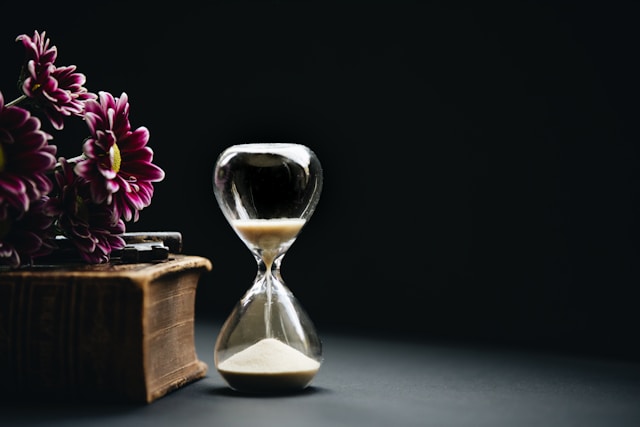 An hourglass next to a wooden box and purple flowers