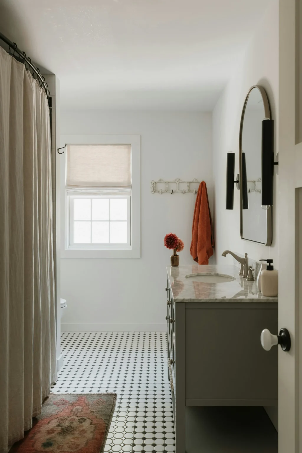 Traditional bathroom remodel in Vancouver by Quay Construction featuring black and white patterned tile flooring, a marble vanity, and an arched mirror.