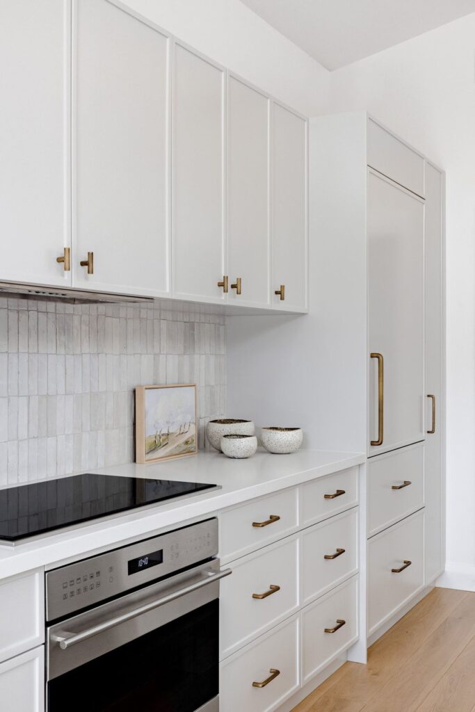 White rock kitchen renovation with white shaker cabinets, brushed gold hardware, vertical subway tile backsplash, and built-in appliances