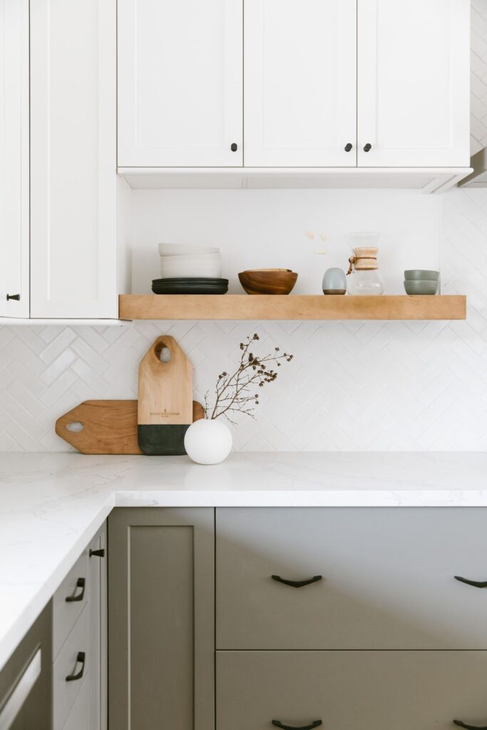 Bright kitchen with white cabinets, wood open shelving, herringbone backsplash, and light quartz countertops.