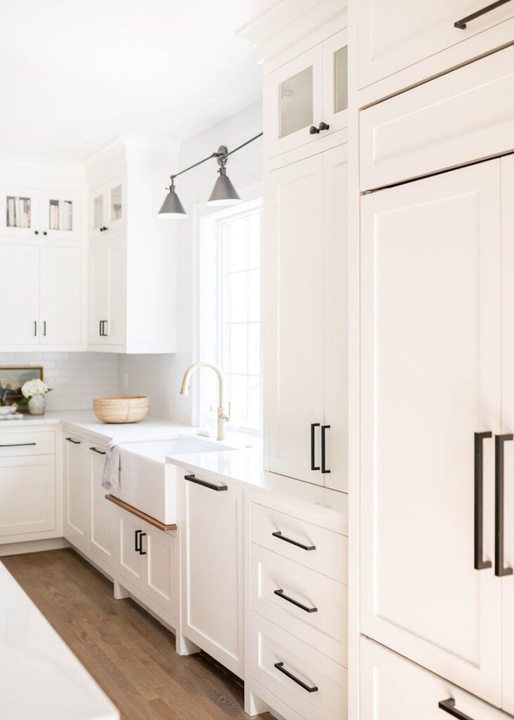 Classic Coquitlam kitchen design featuring white shaker cabinets, a white apron-front farmhouse sink, matte black hardware, and a panel-ready integrated refrigerator.