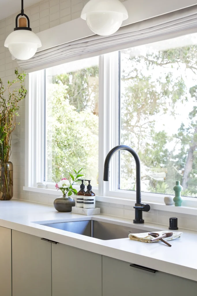 A modern kitchen renovation in Vancouver by Quay Construction featuring a stainless steel undermount sink, a sleek matte black gooseneck faucet, and a bright white countertop in front of a large window with natural views.