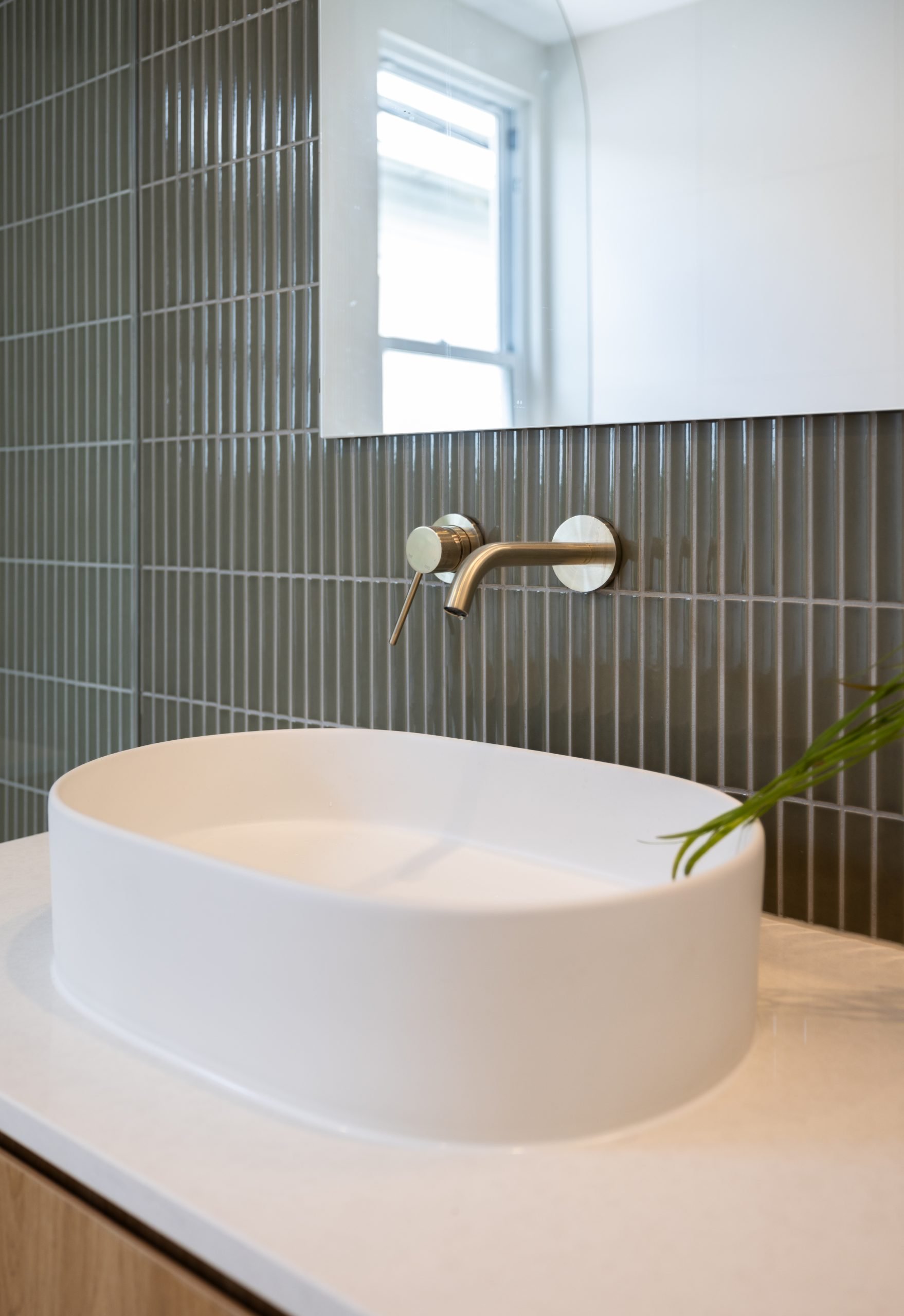 A wall-mounted gold faucet and white vessel sink against grey kit-kat tiles in a home renovation in Edmonds, Burnaby.