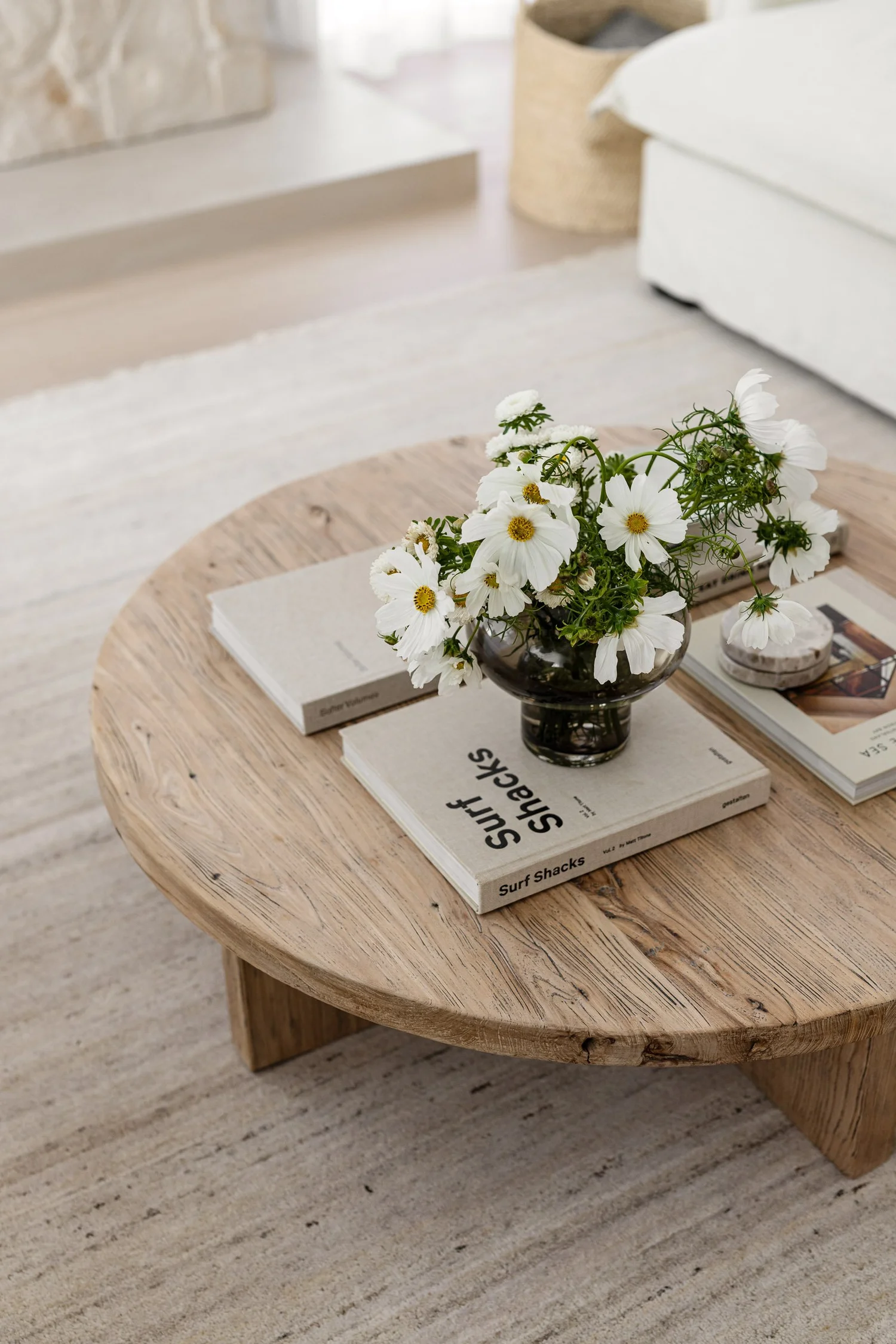 Organic modern living room styling in West Vancouver featuring a reclaimed wood coffee table, white wildflowers in a smoked glass vase, and designer coffee table books on a textured neutral rug.