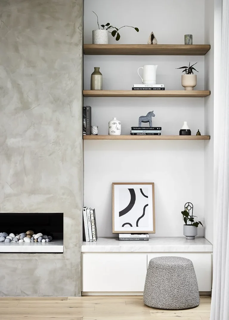 A modern living room from a home renovation in Renfrew–Collingwood featuring a concrete-finish fireplace, custom oak floating shelves, and minimalist white cabinetry.