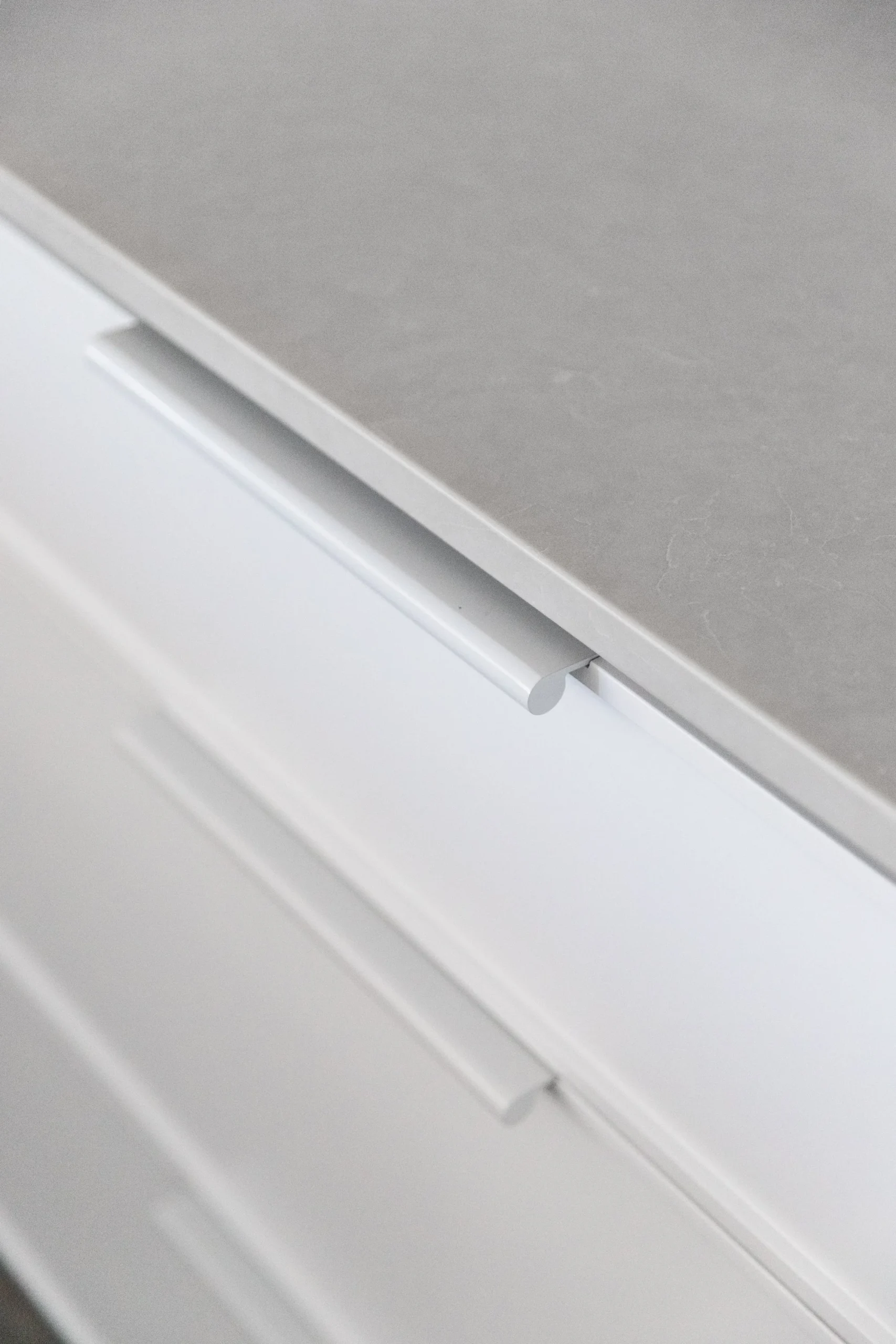 Detail of a modern kitchen remodel in Surrey BC by Quay Construction featuring a grey stone countertop and sleek white handleless cabinetry.
