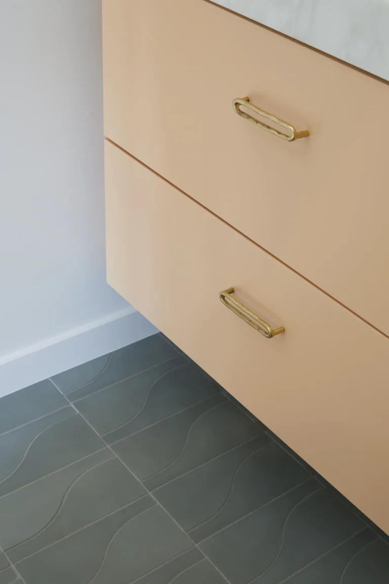 Contemporary basement renovation in Burnaby featuring a peach-colored floating vanity with gold hardware and teal wavy floor tiles by QUAY Construction.