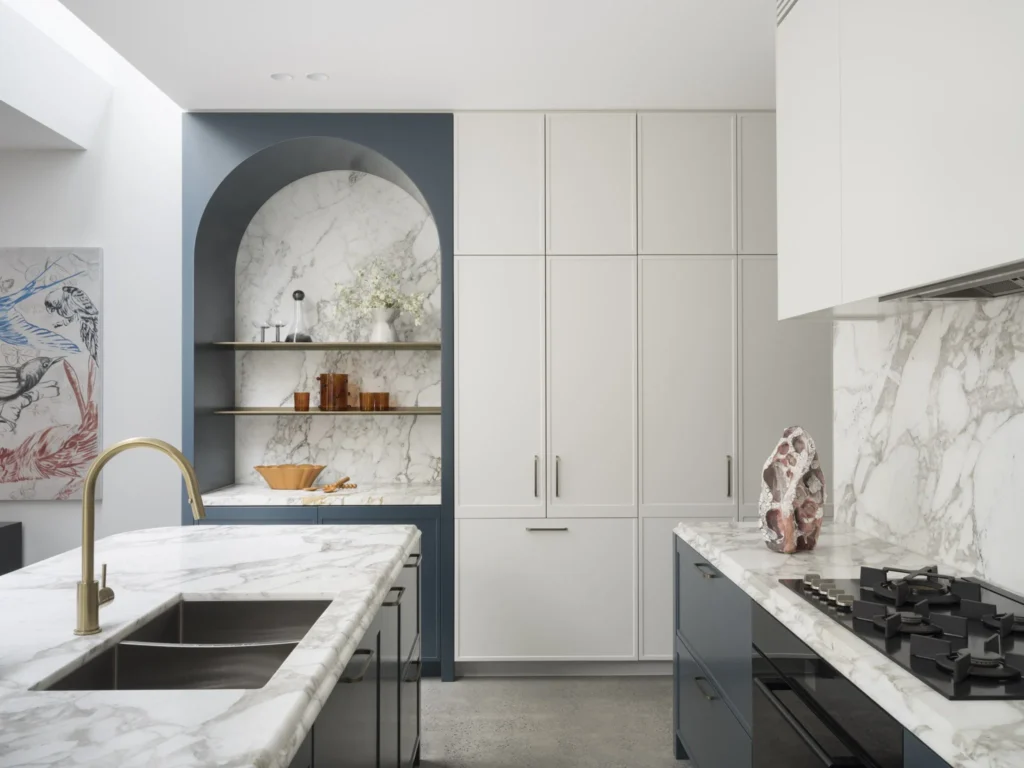 A luxurious kitchen renovation in British Properties featuring deep blue lower cabinets, a marble-backed arched bar area, and white marble countertops.