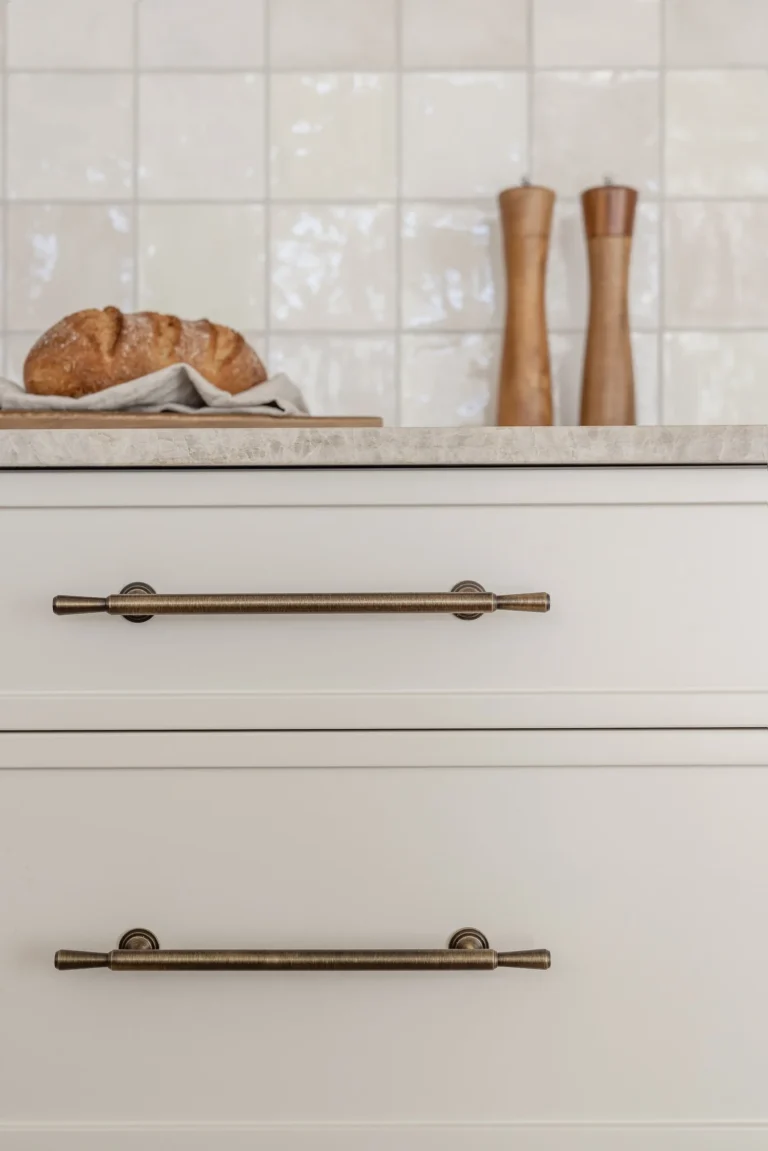 Detail of a Dundarave kitchen renovation showing cream shaker cabinets with antique brass pulls, a marble countertop, and a white Zellige tile backsplash