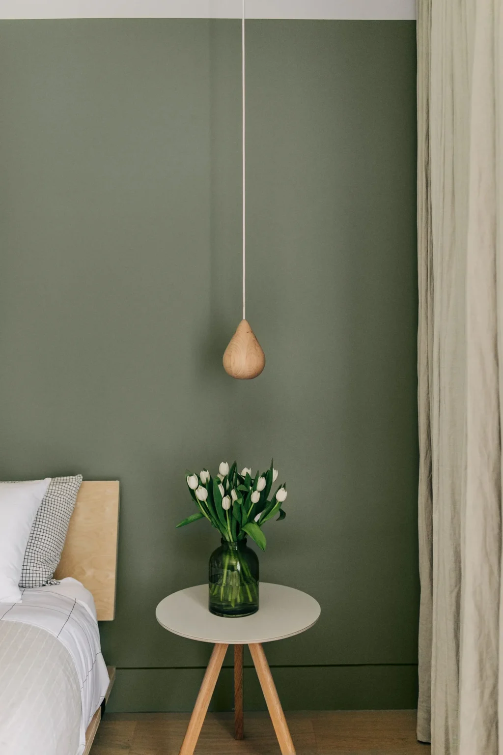 Modern bedroom renovation by Quay Construction featuring a sage green accent wall, wooden pendant light, and minimalist bedside table.