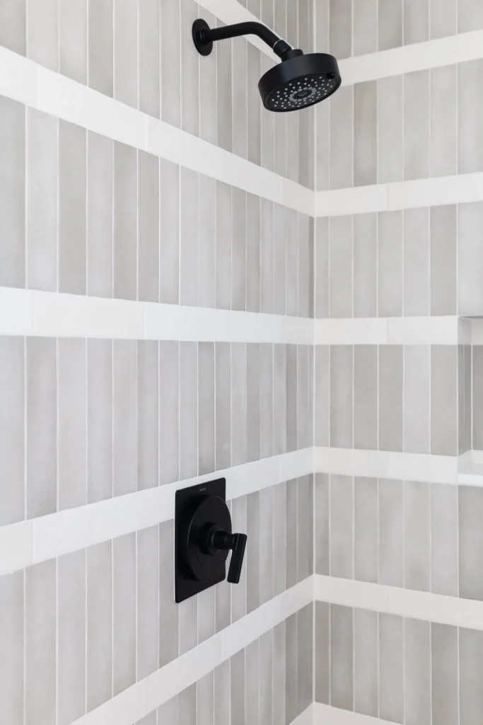 Modern shower renovation by Quay Construction featuring vertical grey subway tiles with white horizontal accents and matte black fixtures.