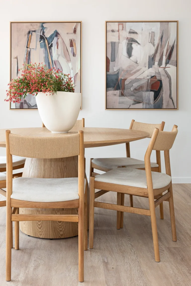 A modern dining room from a home renovation in Marpole featuring a round light oak table, woven chairs, and abstract wall art.