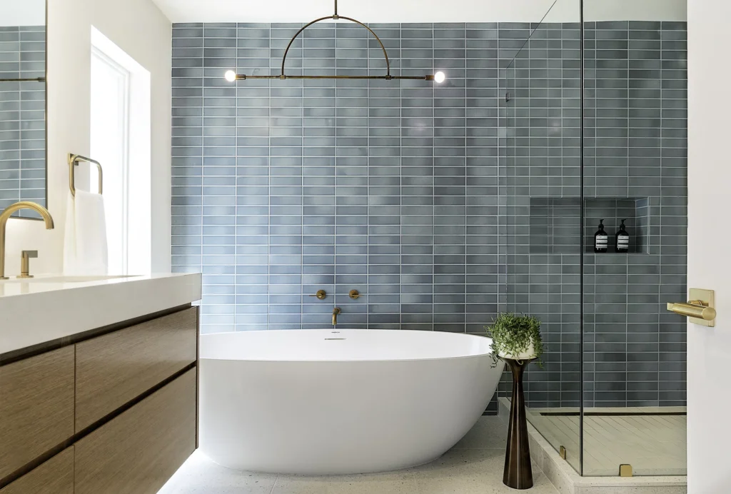 A luxury bathroom from a home renovation in Yaletown featuring a freestanding white soaking tub, blue vertical subway tile accent wall, and a modern gold chandelier.