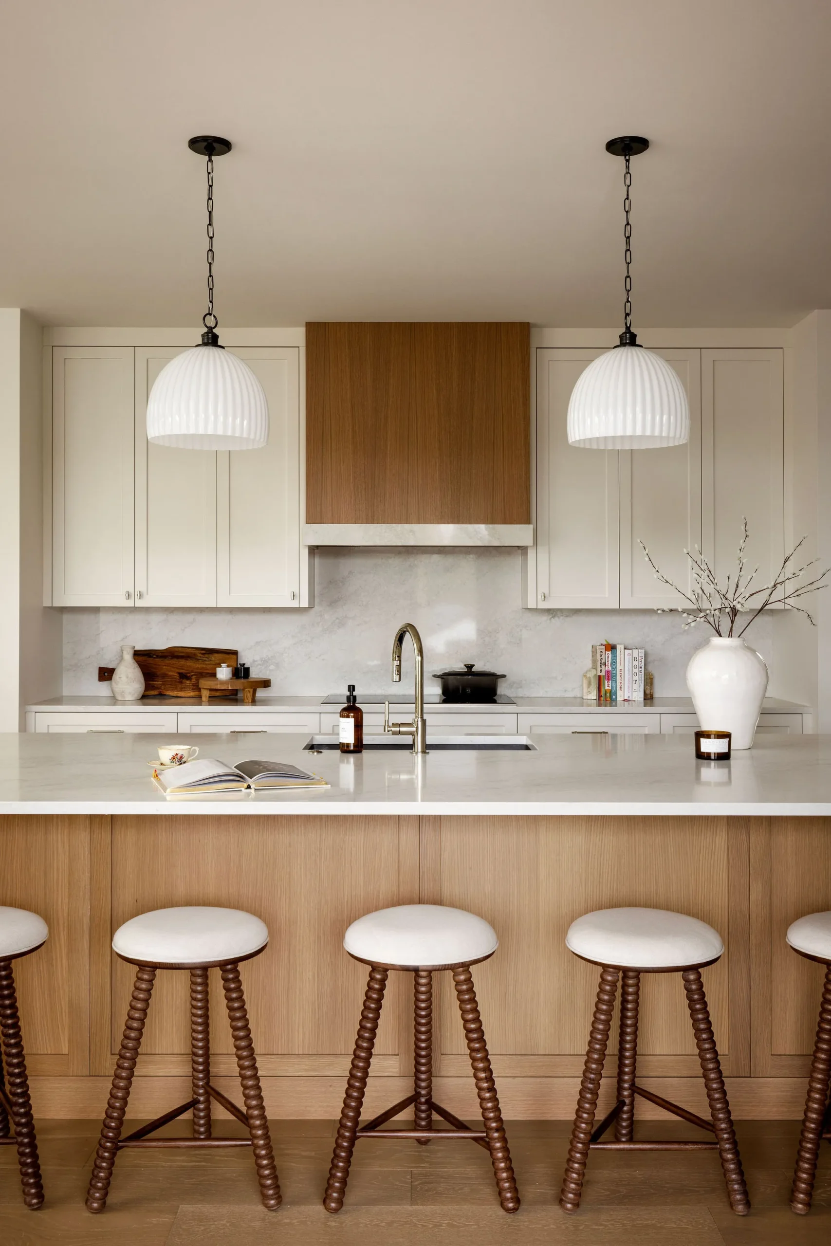 Luxury kitchen renovation Vancouver featuring a large wood island, white pendant lights, and marble backsplash.