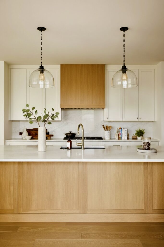 Modern kitchen renovation Vancouver featuring white cabinets, an oak island, marble backsplash, and glass pendant lights.