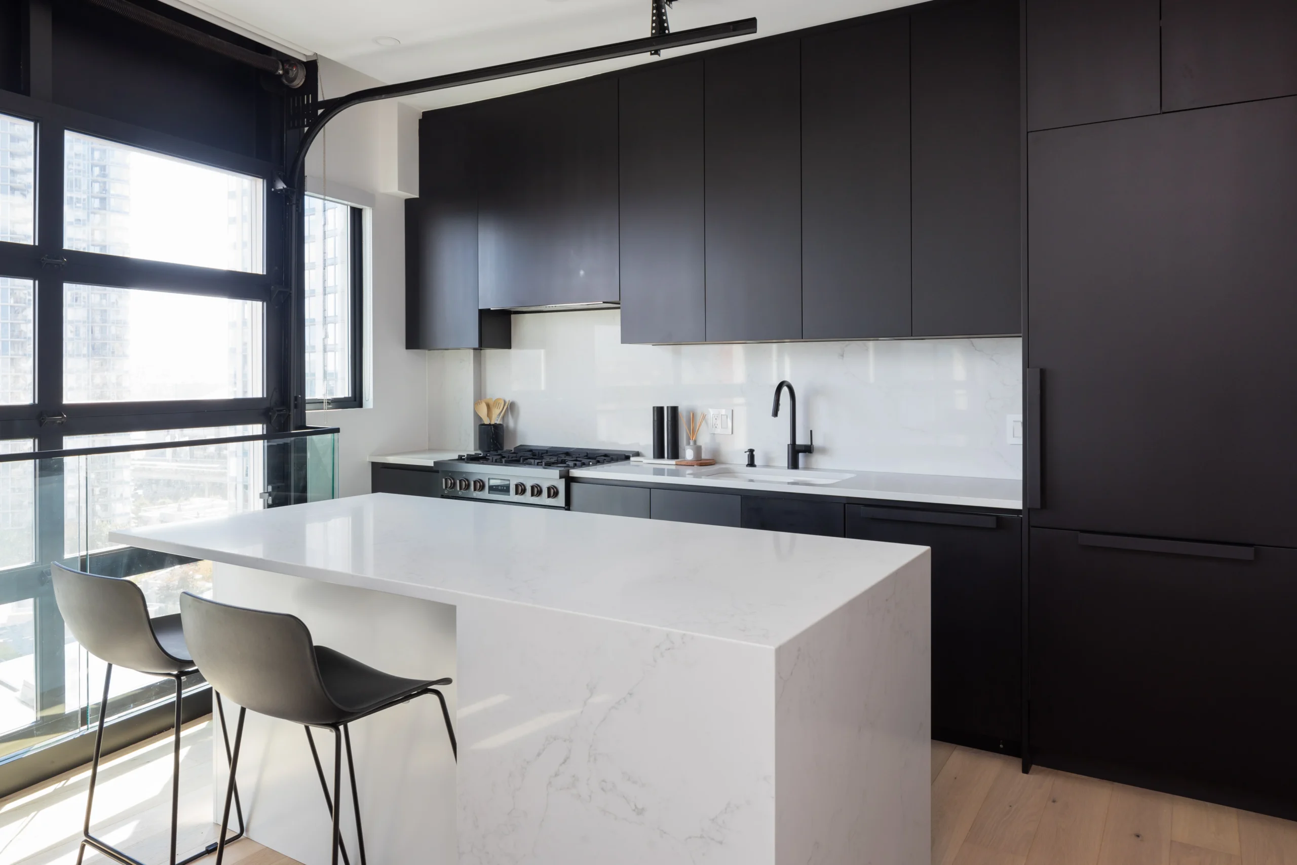 Modern kitchen renovation in Vancouver by QUAY Construction featuring matte black flat-panel cabinetry, white quartz countertops, and a full-height stone slab backsplash.