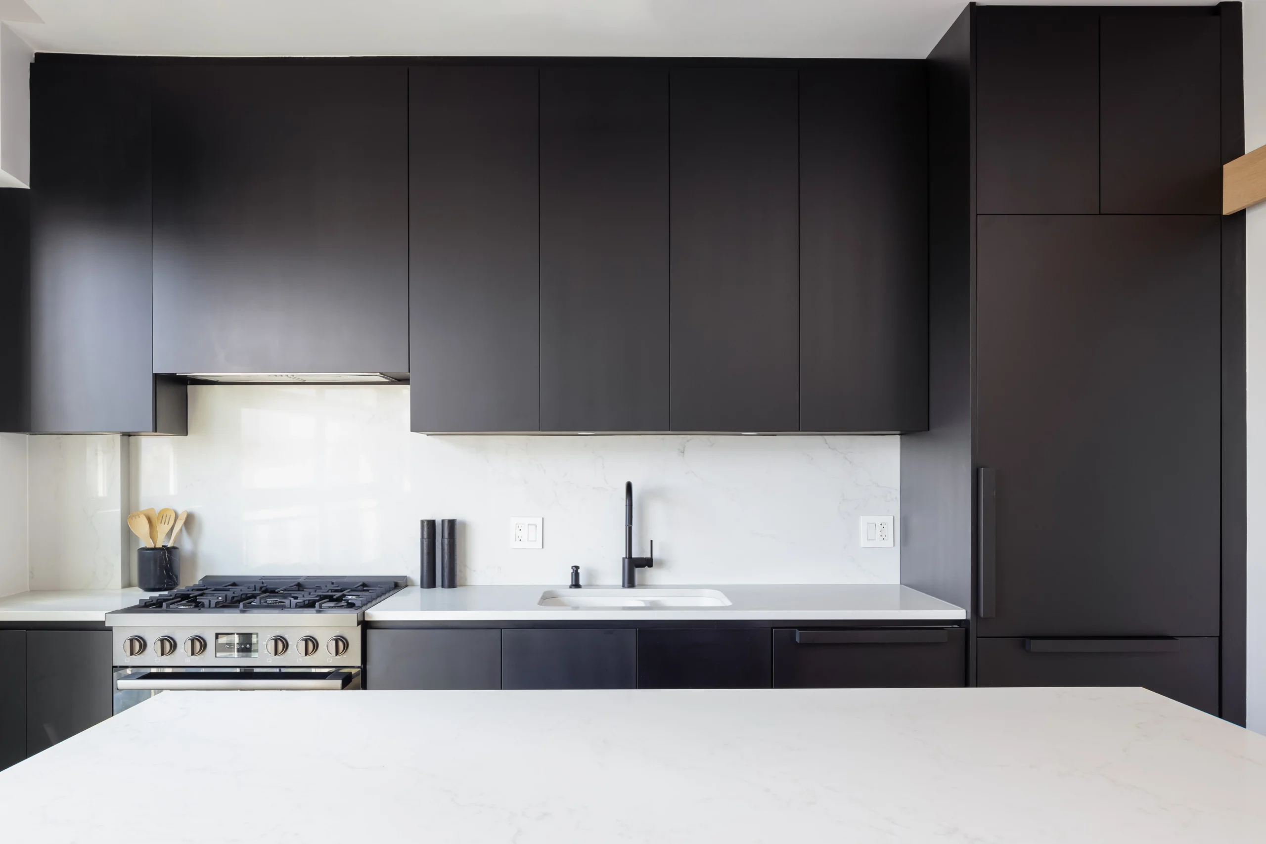 Modern kitchen renovation in North Vancouver by QUAY Construction featuring matte black cabinetry, white quartz countertops, and a matching solid stone slab backsplash.