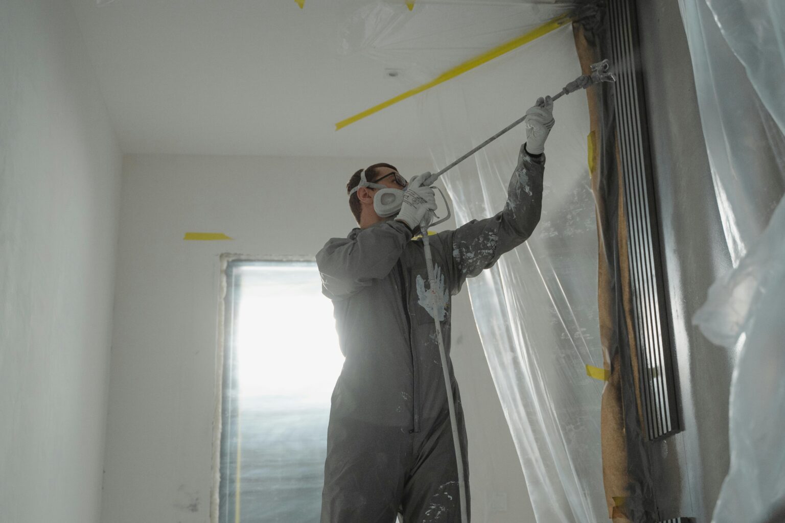 Professional painter applying Benjamin Moore white paint colors 2026 to a luxury interior ceiling using a spray gun.
