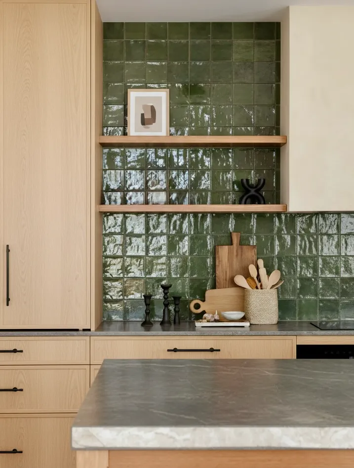 Modern kitchen renovation in Richmond by QUAY Construction featuring light oak wood cabinetry, a glossy green square tile backsplash, and floating wood shelves.
