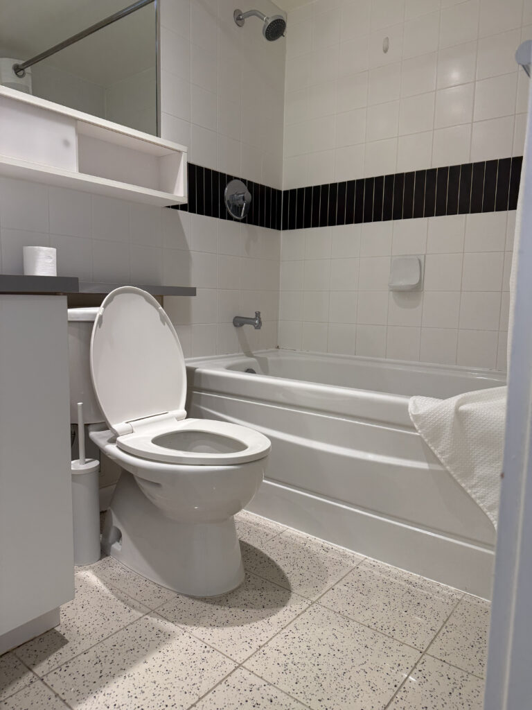 Original Yaletown condo bathroom before renovation featuring builder-grade tile, bathtub shower combination, curtain enclosure, and older flooring.