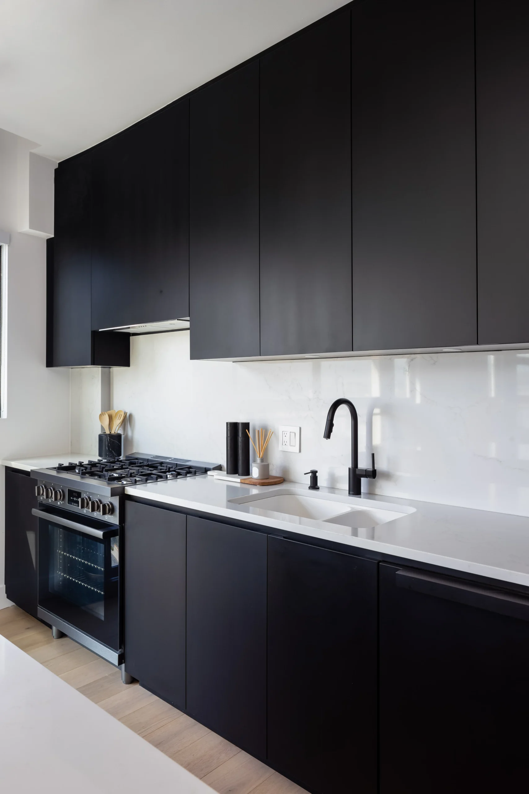 Modern kitchen renovation in Vancouver featuring custom black cabinets, quartz countertops, integrated backsplash, and premium appliances by QUAY Construction.