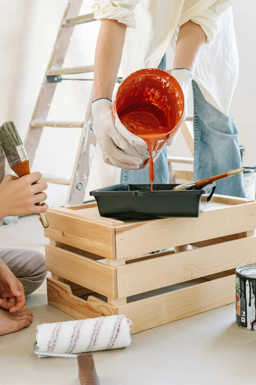 Close-up of orange paint being poured into a tray for a residential renovation, comparing warm vs cool paint colors.