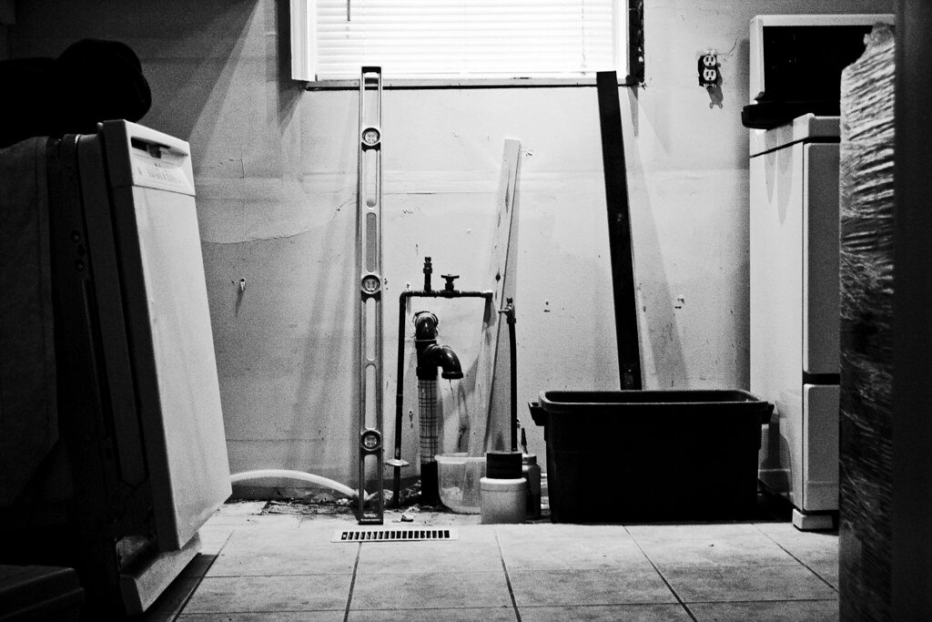 A stripped basement with exposed plumbing pipes, ready for a suite renovation