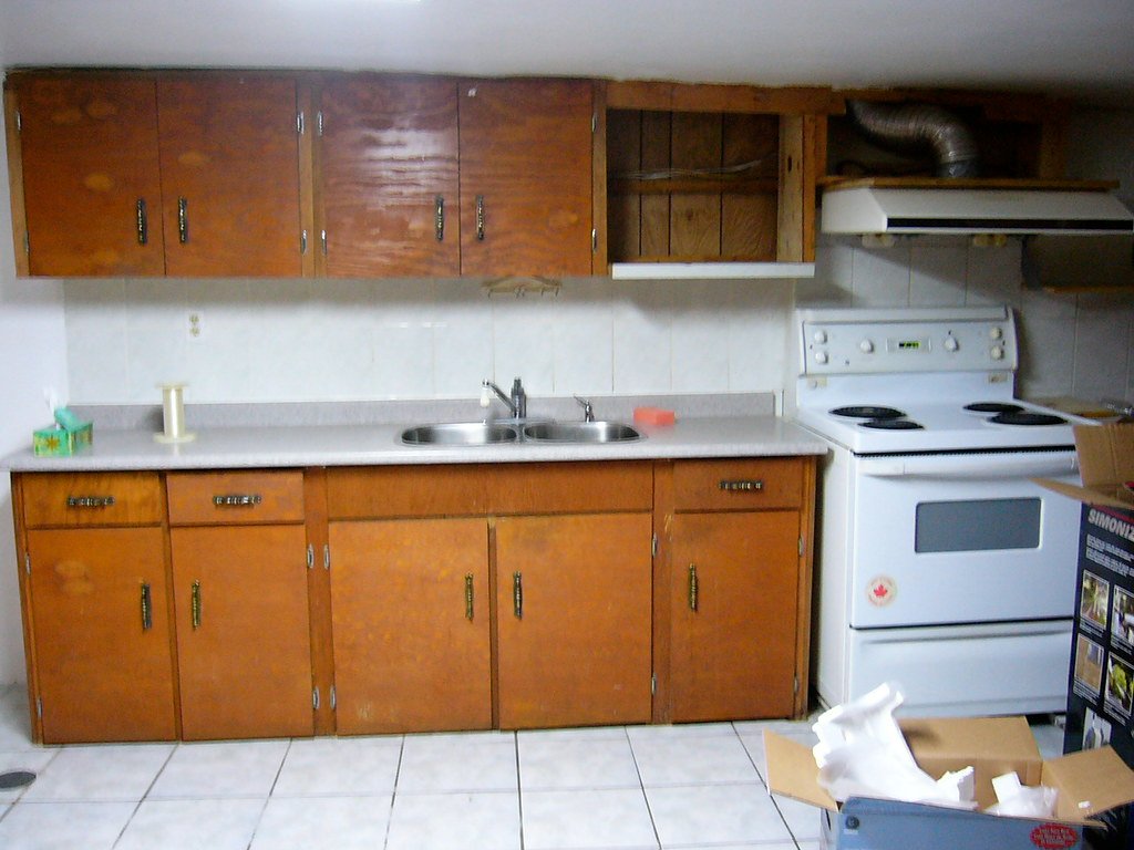 A basement suite kitchen with wood cabinets, a sink, a stove and a range hood