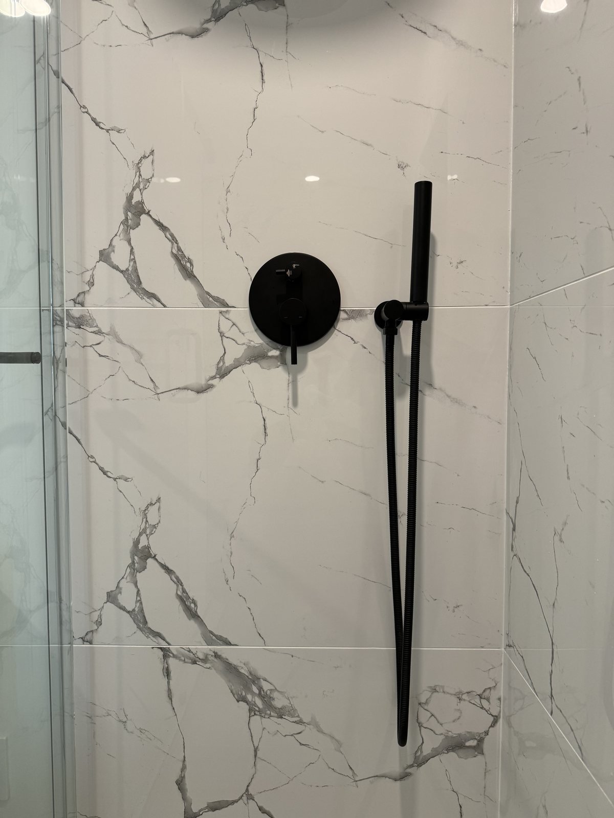 Matte black shower valve and hand shower on large marble-look porcelain tile in a downtown Vancouver condo bathroom