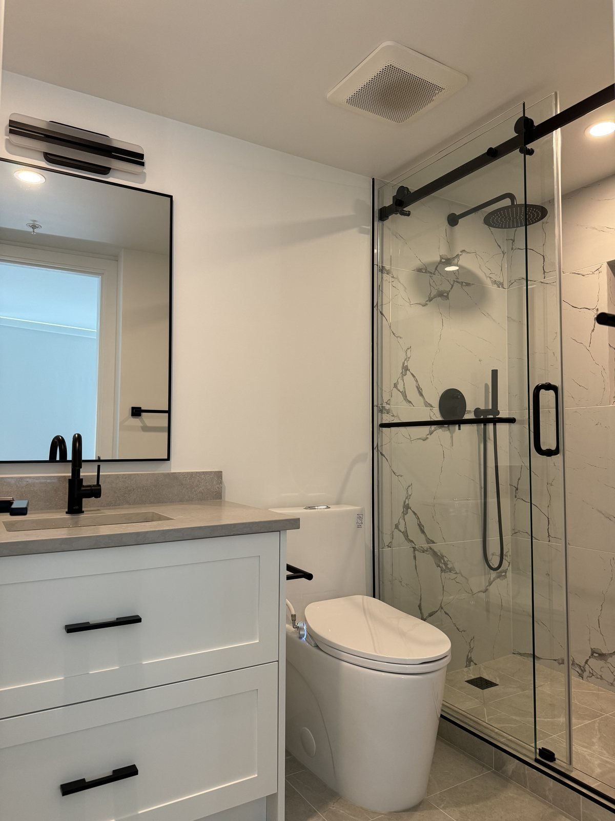 White shaker vanity with a quartz top, black mirror and sliding glass shower in a downtown Vancouver condo ensuite