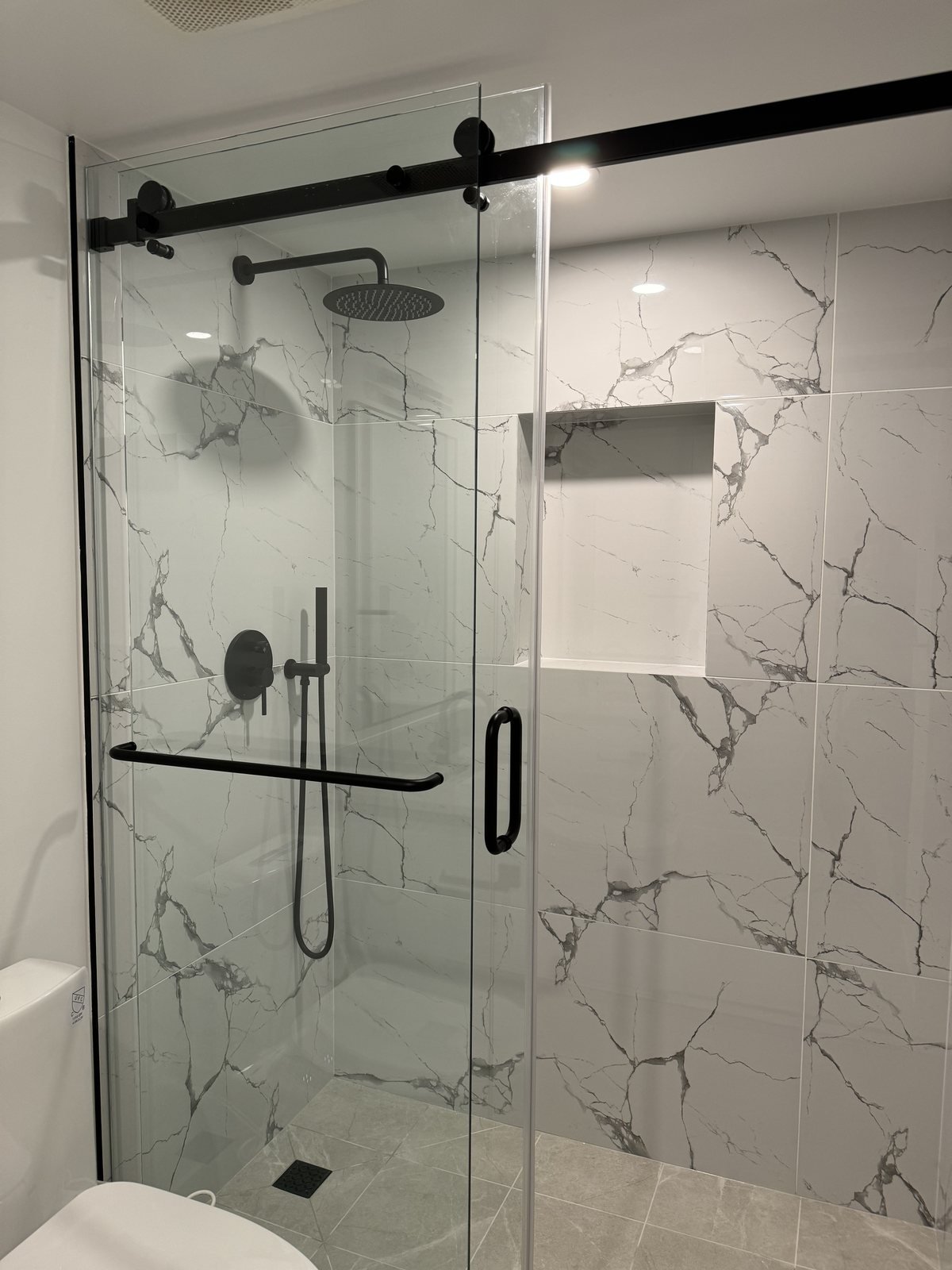 Downtown Vancouver condo ensuite walk-in shower with marble-look tile and matte black fixtures