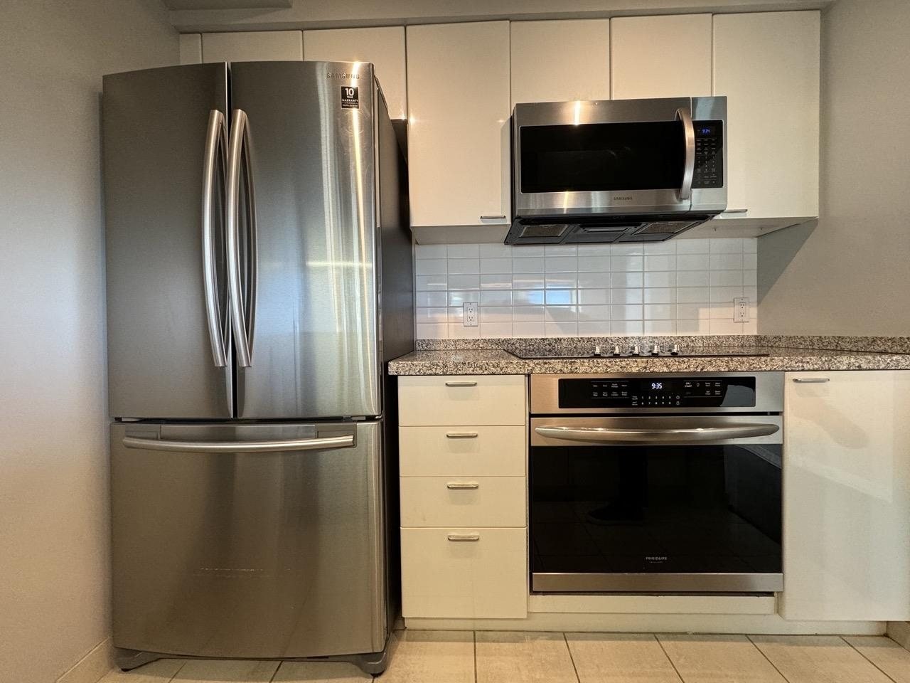Before: galley condo kitchen with white cabinets and a tile backsplash in downtown Vancouver