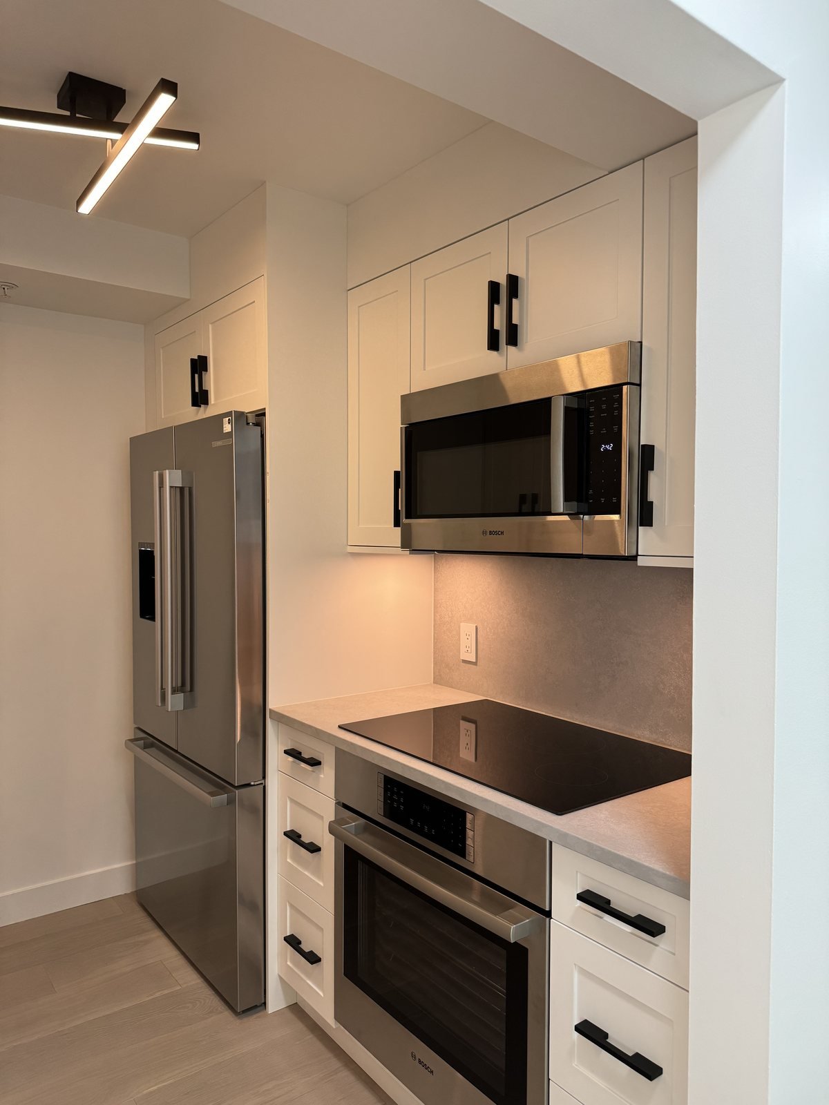 After: galley condo kitchen with stainless appliances, under-cabinet lighting and white shaker cabinets in downtown Vancouver