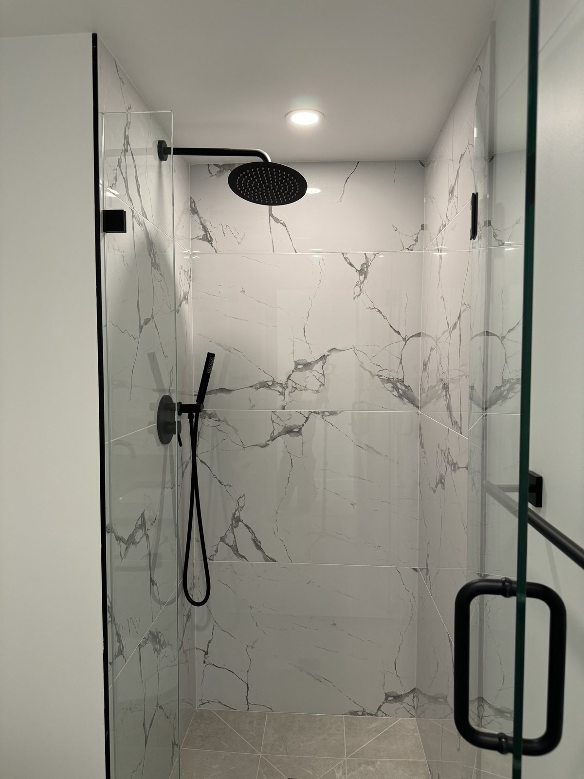 After: main bathroom walk-in shower with a frameless glass door, matte black rain head and marble-look tile in a downtown Vancouver condo