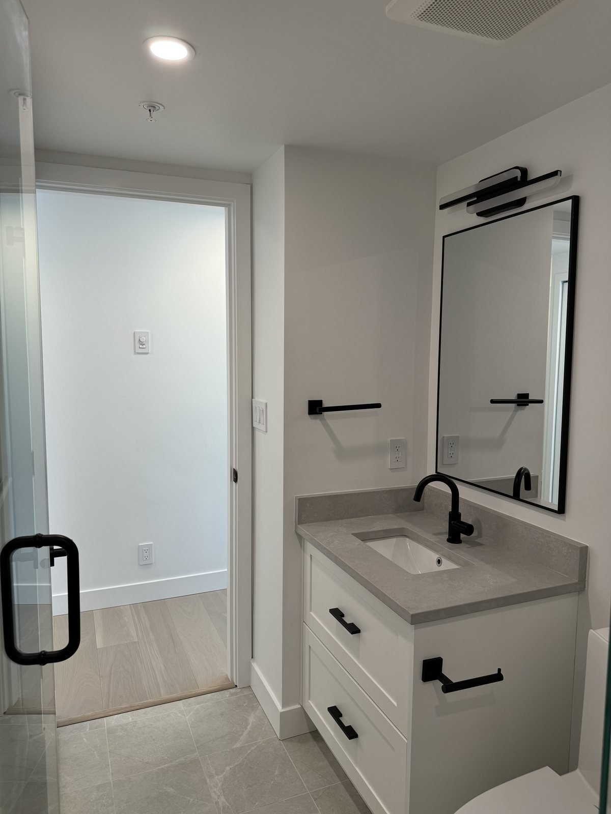 White shaker vanity, quartz top, black faucet and black-framed mirror in a downtown Vancouver condo main bathroom