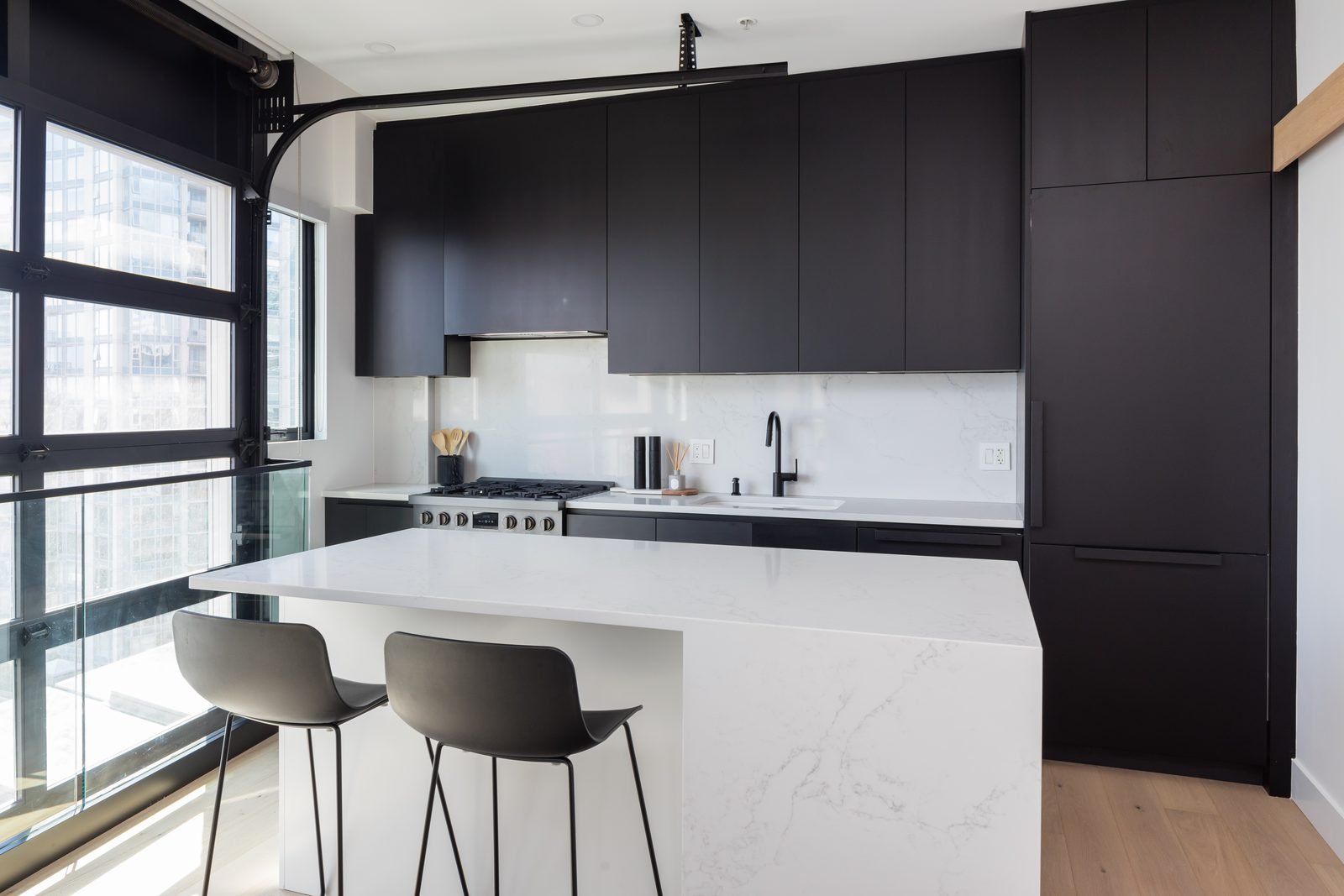 Matte black kitchen with a white quartz waterfall island and loft windows in a Downtown Vancouver condo renovation