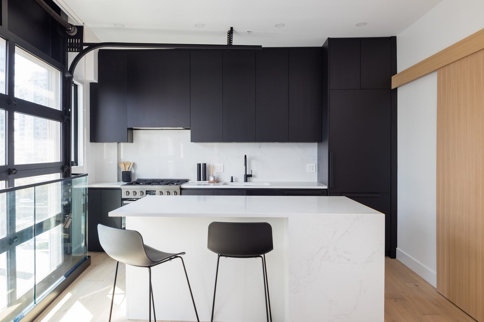 Downtown Vancouver condo loft kitchen with matte black cabinets and a white quartz waterfall island