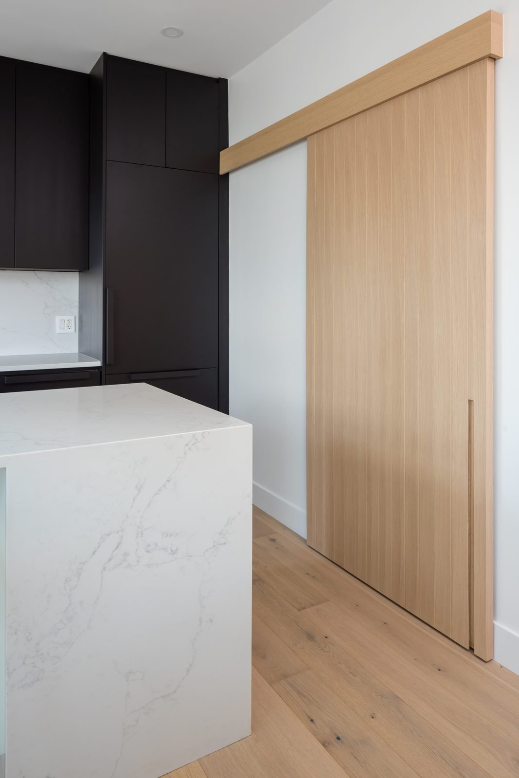 Rift-cut white oak sliding pantry door beside a quartz waterfall island in a Downtown Vancouver kitchen renovation