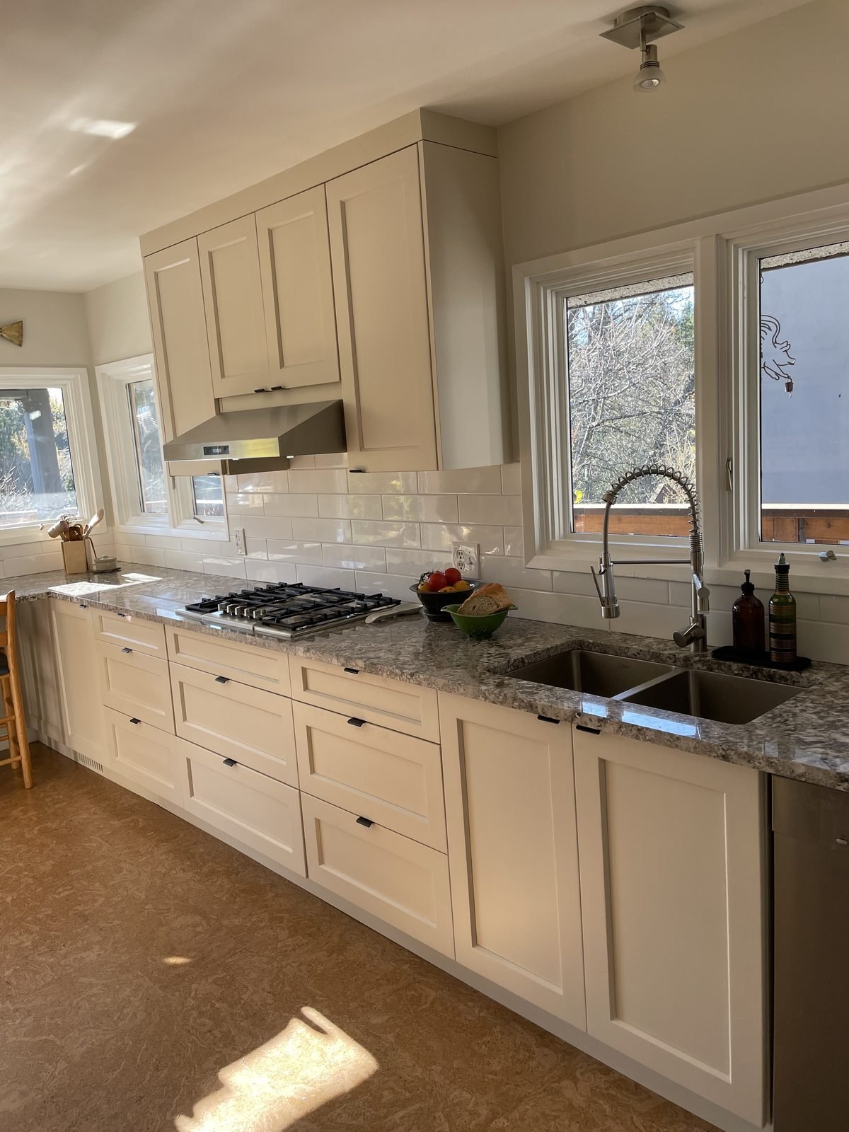 Undermount double sink under the window with grey granite and cream shaker cabinets in a Dunbar, Vancouver kitchen