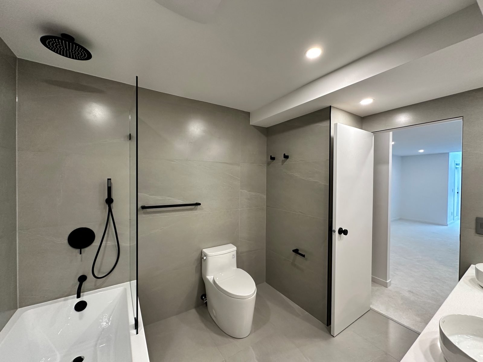 Matte black rain shower and hand shower over a skirted tub, with a one-piece toilet, in a renovated Fairview condo ensuite
