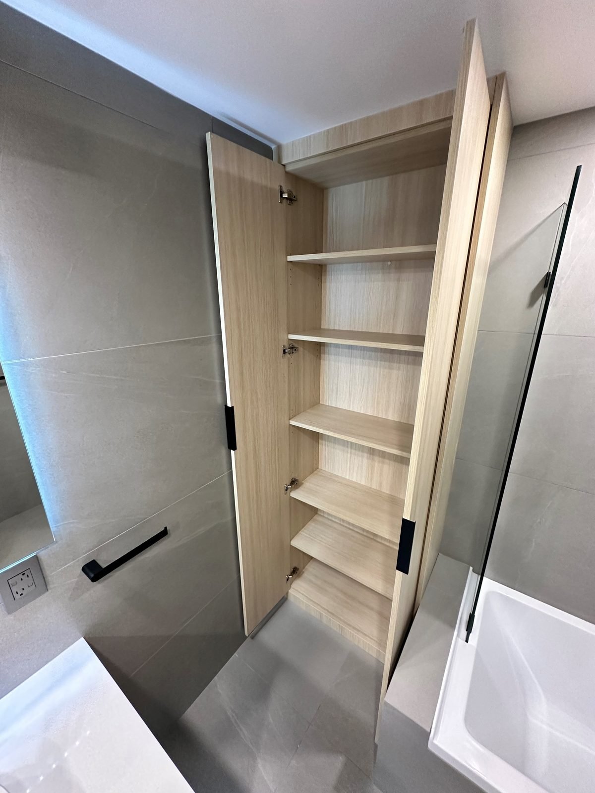 Built-in wood-grain linen cabinet with open shelves beside the tub in a Fairview condo ensuite