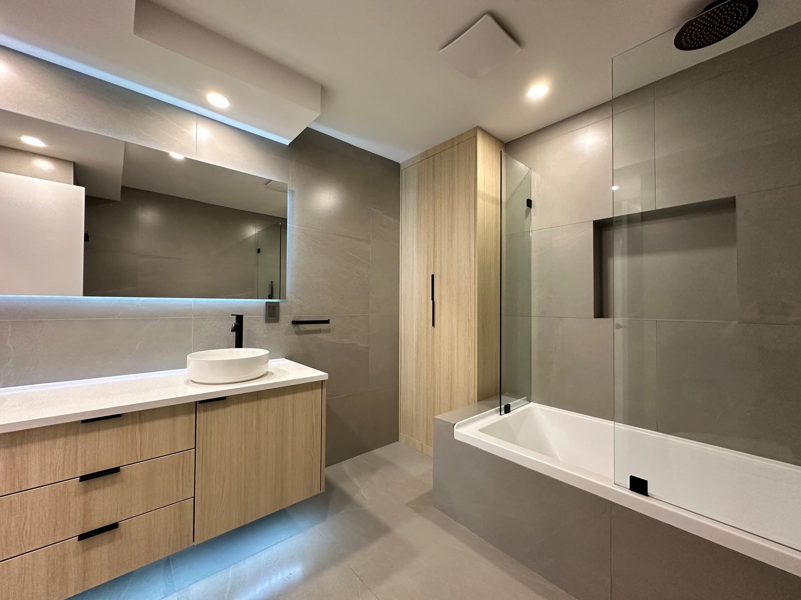 After: skirted tub with a frameless glass panel, tiled niche and built-in linen cabinet in a Fairview condo ensuite