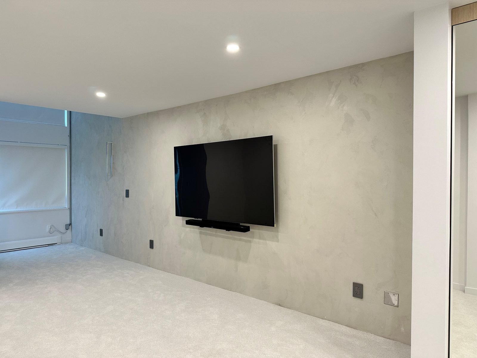 After: primary bedroom with a concrete-finish feature wall, wall-mounted TV and new carpet in a Fairview, Vancouver condo