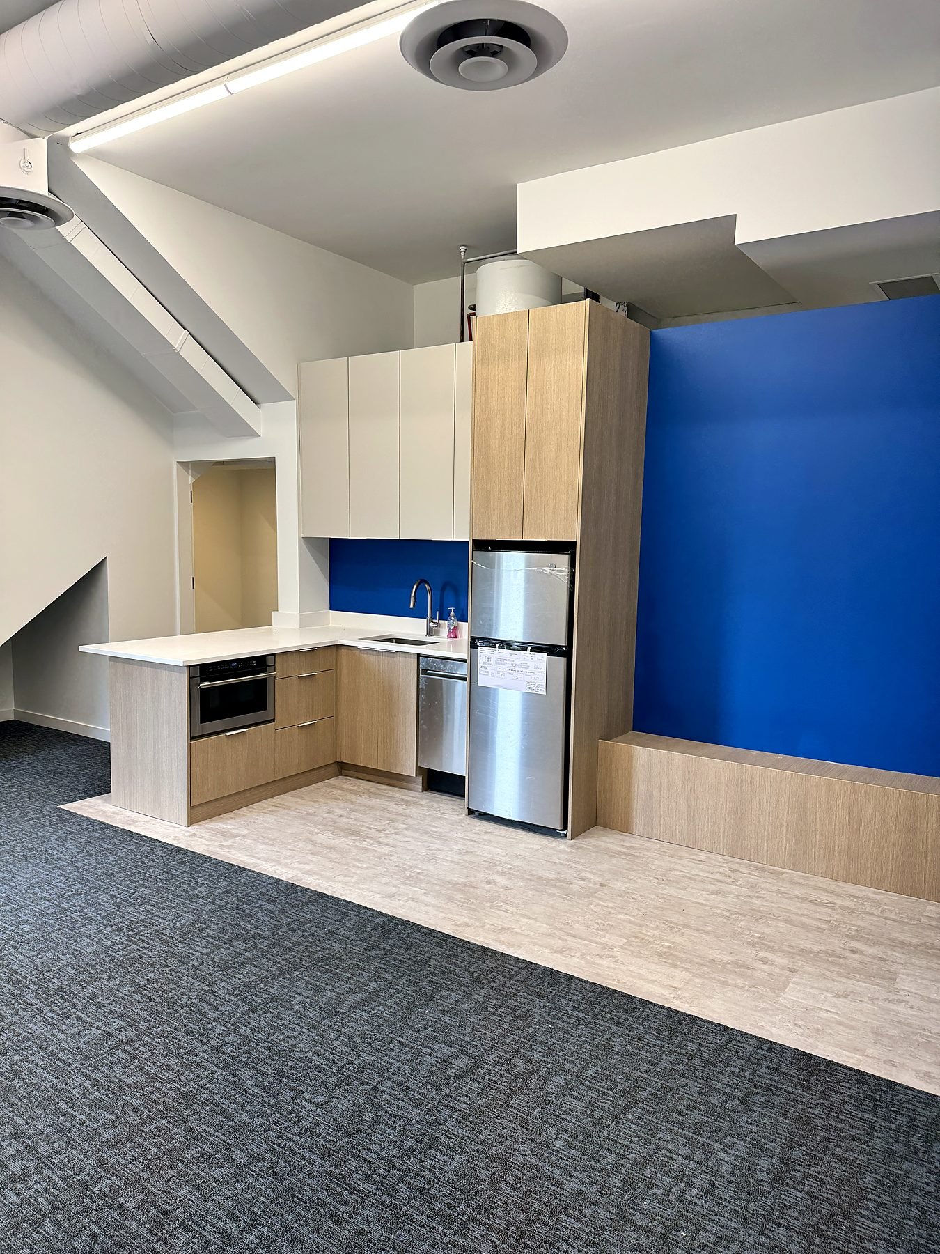 Renovated staff kitchen with blue feature wall, stainless appliances and vinyl plank flooring in a Burnaby office