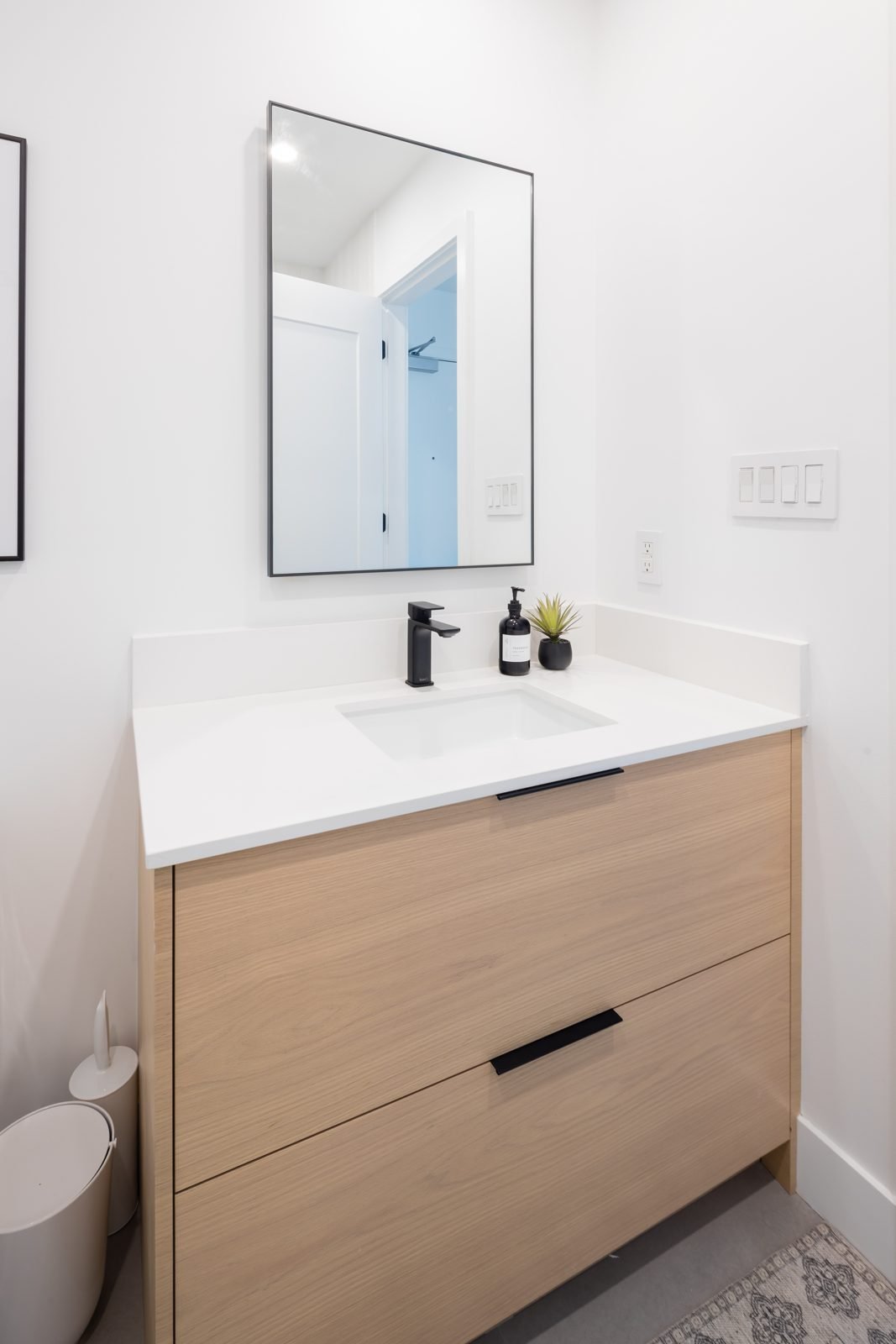 Black-framed rectangular mirror over a white oak vanity with white quartz top in a Gastown condo bathroom