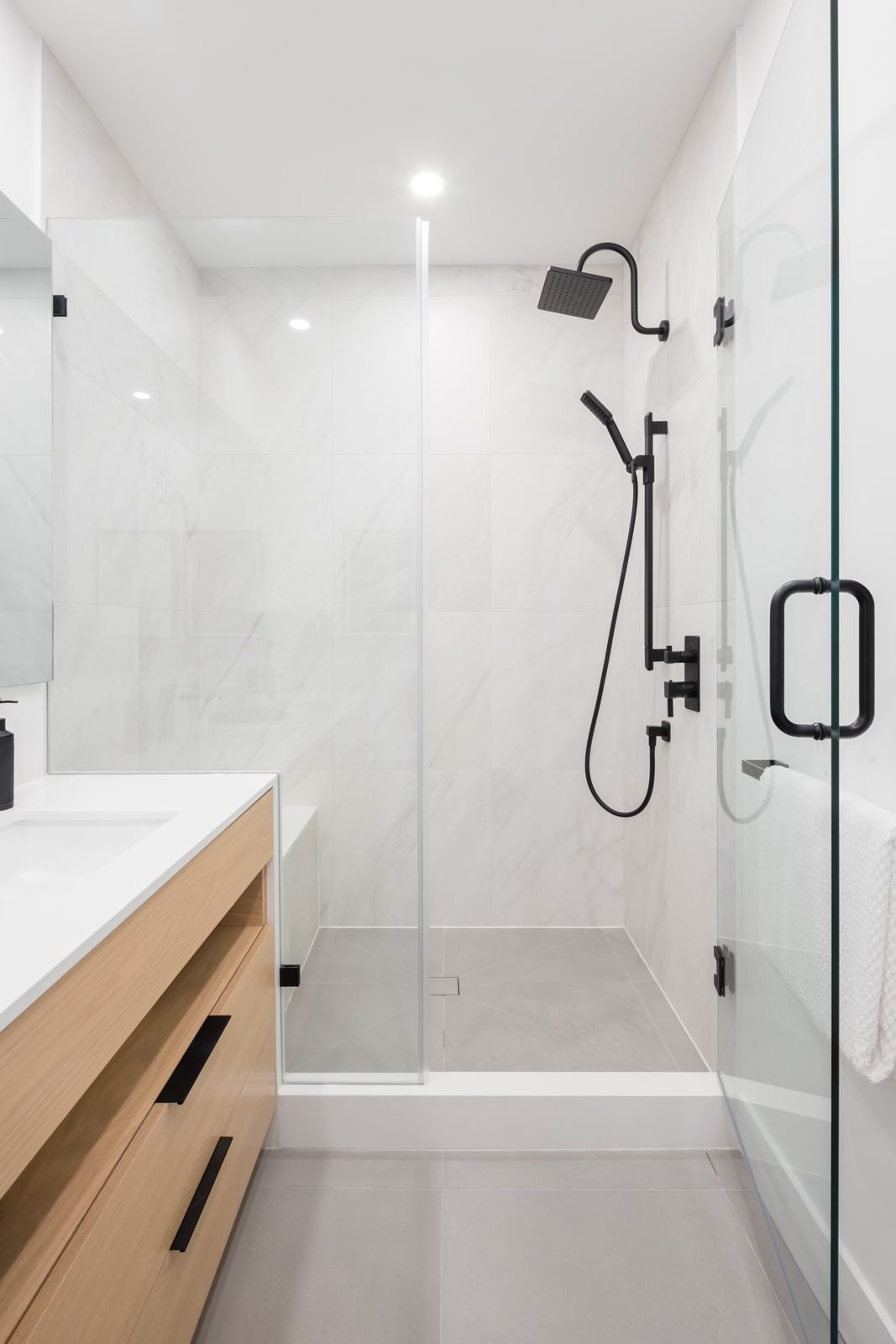 Frameless glass shower with matte black hardware and grey floor tile in a Gastown condo main bathroom