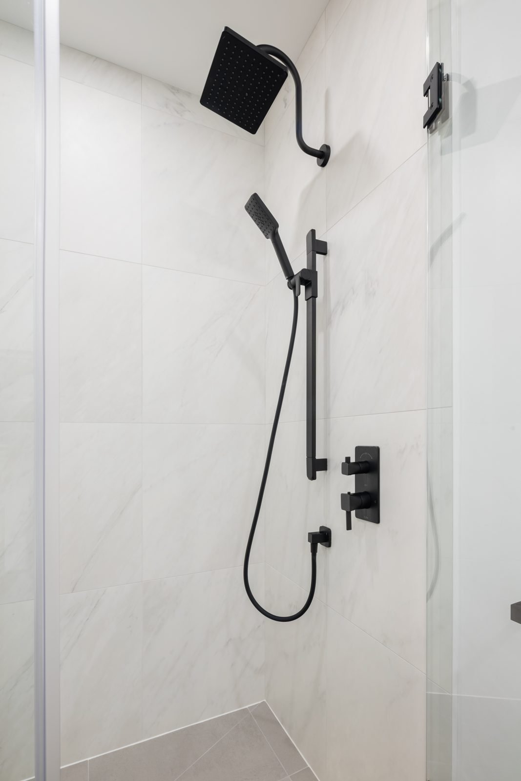 Walk-in shower with stacked white brick-style tile and matte black rain shower in a Gastown condo bathroom